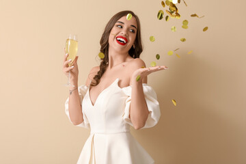 Young woman with glass of champagne and falling confetti on beige background. New Year celebration