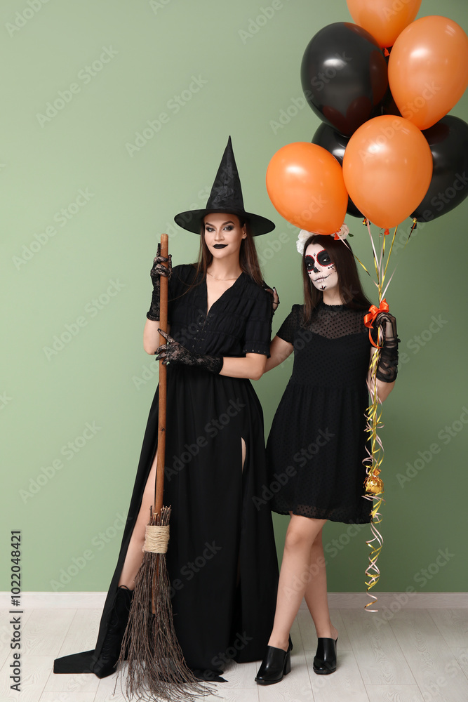 Young women dressed for Halloween with balloons on green background