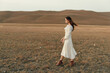 © SHOTPRIME STUDIO - Woman in white dress walking in the middle of open field with mountains in background beauty of nature serenity and solitude