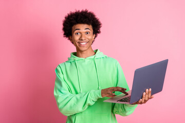 Poster - Photo of nice young man use laptop wear green hoodie isolated on pink color background