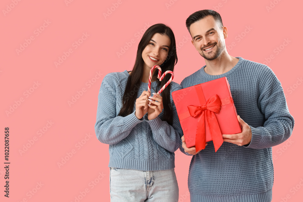 Young couple with Christmas present and candy canes on pink background