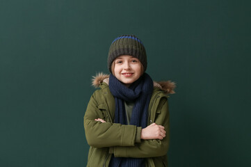 Wall Mural - Cute little happy boy in winter clothes on dark green background