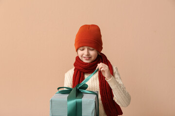 Wall Mural - Cute little happy boy in winter clothes with gift box on beige background