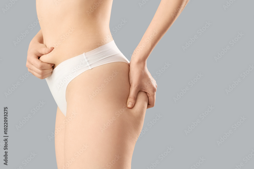 Beautiful young woman in underwear with cellulite problem on grey background