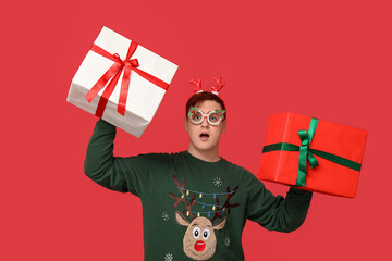 Poster - Handsome young man in warm sweater with gift boxes on red background