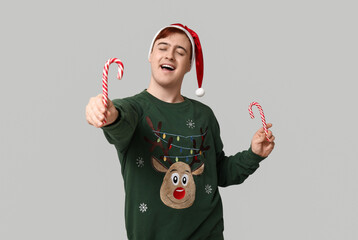 Poster - Handsome young man in warm sweater, Santa hat and candy canes on grey background