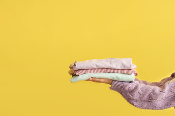 Canvas Print - Woman with folded sweaters on yellow background