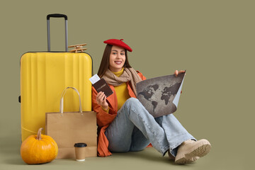 Wall Mural - Female tourist in autumn clothes with travel accessories sitting on green background