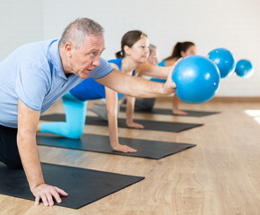 Class of male and women of different ages in active wear working out with mini balls during Pilates training together in rehabilitation center