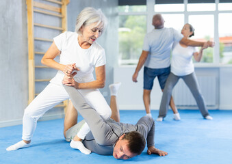 Wall Mural - Mature woman learns how to do painful hold with trainer in the gym. Self-defense lesson