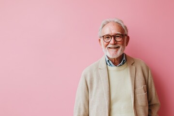 Half body shot of a senior man, smiling warmly, standing against a solid soft pink background with space for text