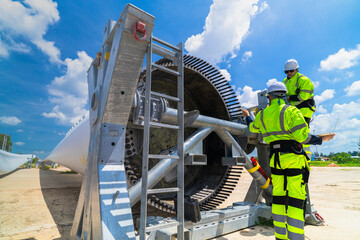 two engineers in safety gear inspecting a wind turbine blade section on a construction site. they ex