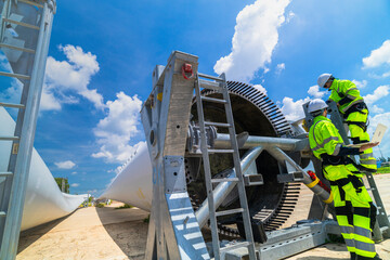 two engineers in safety gear inspecting a wind turbine blade section on a construction site. they ex