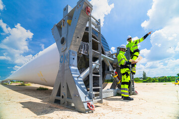 two engineers in safety gear inspecting a wind turbine blade section on a construction site. they ex