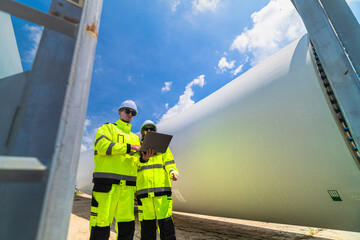 two engineers in safety gear inspecting a wind turbine blade section on a construction site. they ex