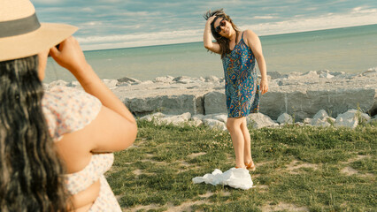 Two women are standing on a grassy field near the ocean