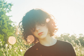 Wall Mural - A woman with curly hair is standing in a field with the sun shining on her