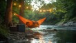 © julio - Cozy hammock by a river with string lights for relaxation.