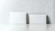 © HQAsset - Two Blank White Cards Mockup on a White Surface with a White Wall Background