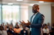 © GustavsMD - Confident black business man in a suit delivering a presentation at a professional conference, engaging the audience with a compelling speech