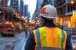 © Trusha - Construction worker wearing a yellow vest and a hard hat stands on a street. The scene is set in a city with a lot of construction going on