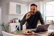 © Drazen - Male entrepreneur eating breakfast while using computer and working at home.