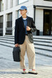 © Seventyfour - Vertical shot of fashionable Asian man wearing black jacket outfit and holding laptop bag while posing in city street captured during daily commute on foot to workplace, copy space