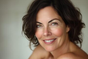 Close-up portrait of a smiling  mature woman with curly hair against a soft, neutral background