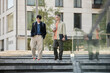 © Seventyfour - Full length shot of two male IT developers in stylish outfits talk business during walking meeting or daily commute to work while descending steps outside in city street, copy space