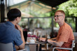 © Seventyfour - Side view of smiling businessman using laptop sitting at cafe table while enjoying talk and collaborate work over cup of coffee with colleague in outdoor seating area of cafe, copy space