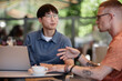 © Seventyfour - Medium shot of smiling Asian man attentively listening to colleague enjoying conversation and collaborate work over cup of coffee while using laptop at cafe table in outdoor seating area, copy space