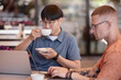 © Seventyfour - Medium shot of Asian male IT programmer looking at laptop screen enjoying hot beverage while working together with colleague during coffee break at cafe table, copy space