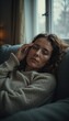 © Yosich1961 - Weary woman reclining on worn couch rubbing her eyes with soft diffused light from cloudy winter day