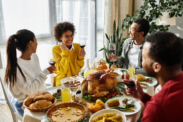 A group of friends gather around the table enjoying Thanksgiving dinner with smiles and toasts.