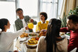 © LIGHTFIELD STUDIOS - Friends toast glasses and share laughter while enjoying a Thanksgiving feast together at home.