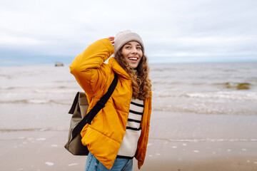 young woman tourist walking beach on cloudy day. autumn near the sea. travel, tourism concept. activ