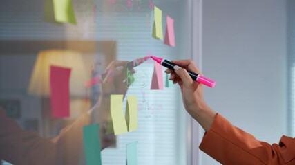 Wall Mural - businesswoman is drawing on a transparent glass whiteboard with a pink marker during a business meet