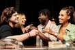 © LIGHTFIELD STUDIOS - Diverse group of young professionals share laughter and drinks at a festive party atmosphere.