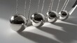 © KYR - Close-up of a silver Newton's cradle on a simple background, representing the physics of energy transfer and the balance