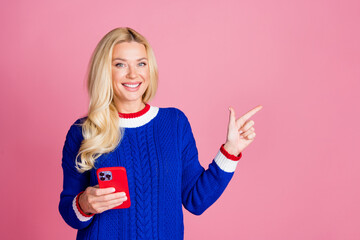 Sticker - Photo of pretty lady hold smart phone point finger empty space wear blue sweater isolated on pink color background