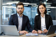 © Liubomir - Business professionals sitting in office with laptops looking confident. Teamwork concept featuring modern technology, collaboration, and productivity in corporate environment.