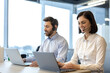 © Liubomir - Business professionals using headsets while working on laptops in office setting. Call center employees discussing client communication, focused on providing excellent customer service.