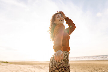 Beautiful woman at the windy day walks along the beach and enjoys the autumn weather. Travel, weekend, relax and lifestyle concept.