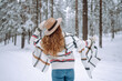 © maxbelchenko - Back view of woman standing among snowy trees in winter forest and enjoying first snow. Wearing hat, plaid scarf and coat. Wanderlust and boho style