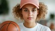 © Pinklife - A focused young woman wearing a pink cap and casual outfit is holding a basketball with a confident expression, emphasizing athleticism and youthful determination.