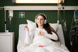 © ABCreative - Enjoying music, the patient wears headphones in her comfy bed in hospital ward.