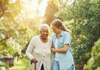 young woman volunteer assisting happy senior woman with walking stick in a garden