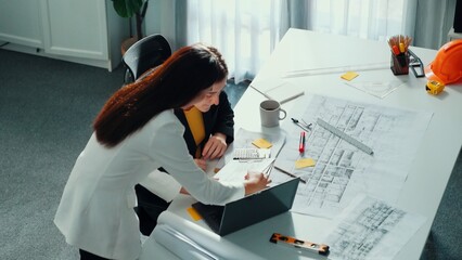 Top view of smart business woman talking and give house design. Aerial view of architect engineer looking at blueprint and building structure at table with safety helmet and house model. Alimentation.