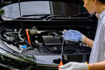 A close-up of young woman checking engine oil level at home before a road trip for safety of car and passengers.