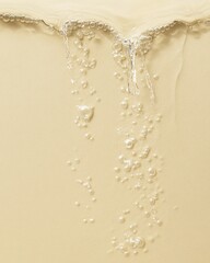 Close-up of flowing liquid with bubbles over a creamy beige surface, highlighting a smooth and refreshing texture ideal for skincare or beauty products.